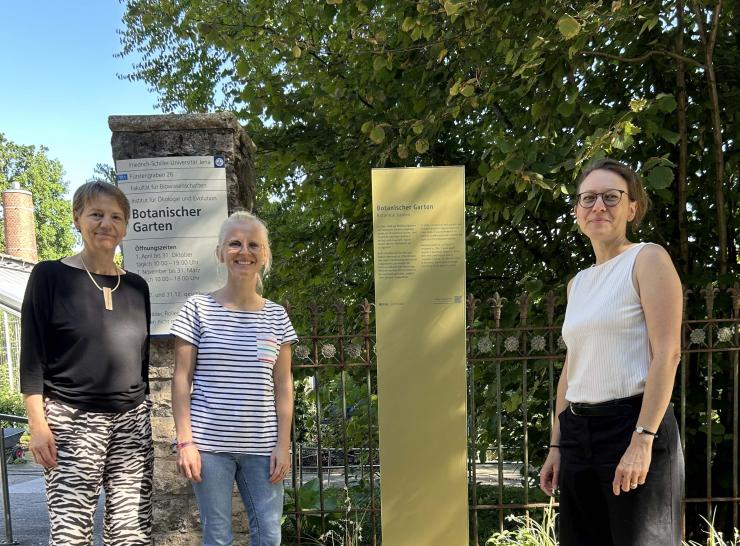 Drei Personen stehen neben einer Stele