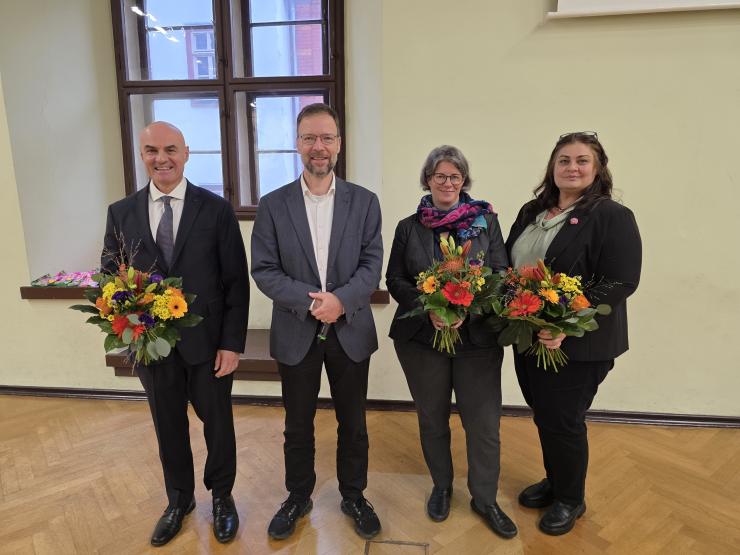 Vier Menschen stehen nebeneinander, drei von ihnen haben einen Blumenstrauß in den Händen
