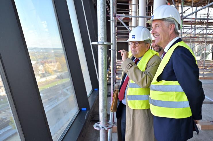 Zwei Männer mit Sicherheitsweste und -helm besuchen eine Baustelle und blicken aus dem Fenster
