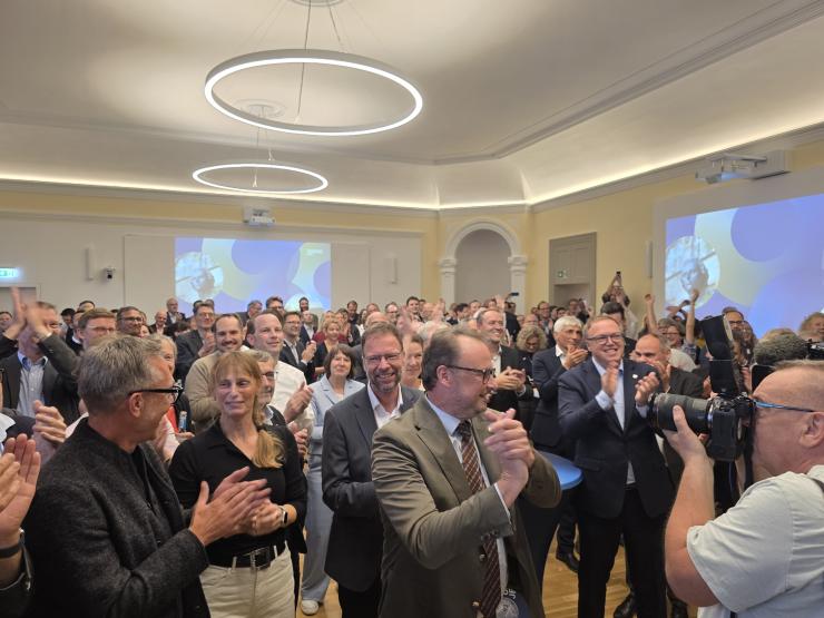 Menschen stehen in einem Saal und klatschen in die Hände.