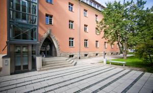 Blick auf ein orangefarbenes Gebäude. Der Eingang und der außen angebrachte Fahrstuhlbau ist sichtbar.