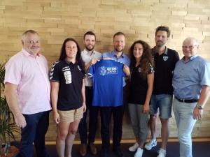 Fünd Männer und zwei Frauen halten ein Fußball-Trikot in die Kamera.