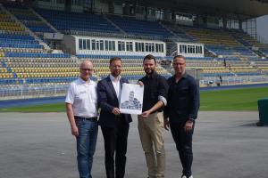 Karl-Hermann Kliewe, Dr. Thomas Nitzsche, Benjamin Koppe und Carsten Müller halten im Stadion einen Zettelmit dem neuen Logo