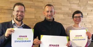 Drei Menschen halten Plakate in die Kamera