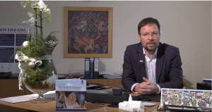 Video-Screenshot: OB sitzt an seinem Schreibtisch 