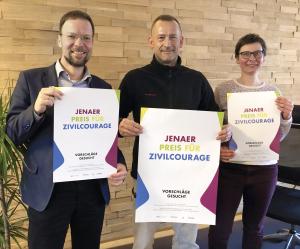 Drei Menschen halten Plakate in die Kamera