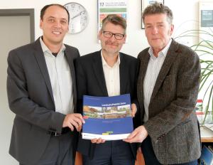 Drei Männer halten ein Buch in die Kamera