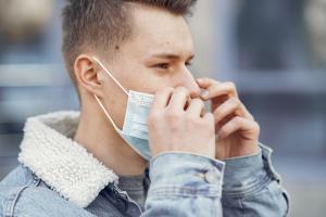 Junger Mann setzt Mund-Nasen-Bedeckung im Freien ab