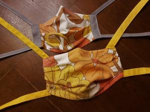 Zwei selbstgenähte Mund-Nasen-Bedeckungen in bunten Farben liegen auf einem Holztisch