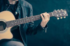 Person hat eine Gitarre auf dem Schoß und spielt sie