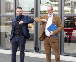 Zwei Männer vor einer Garage stoßen die Ellenbogen zusammen