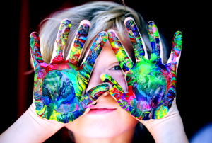 Ein Kind mit angemalten Händen schaut in die Kamera