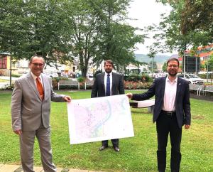 Drei Personen stehen auf einer Wiese und halten eine Karte in der Hand. Im Hintergrund sind Gebäude zu sehen.