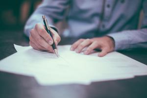 Hand mit Stift unterschreibt auf einem Blatt Papier.