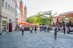 Blick in eine Straße: links und rechts sind Häuser, im Hintergrund ist die Jenaer Stadtkirche zu sehen, im Vordergrund laufen Menschen durch die Straße