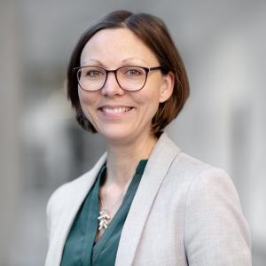 Frau Braune steht im Außenbereich, der Hintergrund des Bildes ist verschwommen.