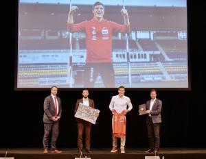 Vier Männer auf ein Bühne, im Hintergrund ein großes Bild eines Sportlers