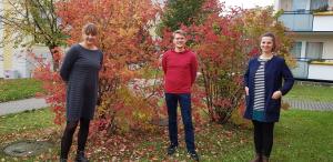 Zwei Frauen und ein Mann stehen im Herbst vor einem Busch.