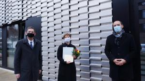 Zwei Herrn und eine Dame schauen in die Kamera. Im Hintergrund eine Fassade aus Metall.