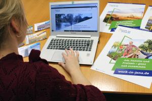 Eine Frau sitzt an einem Laptop auf der eine Internetseite zu sehen ist