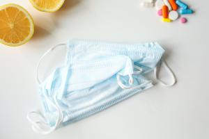 Hellblaue OP-Masken, Zitronenscheiben und einige Tabletten liegen auf einer hellen Fläche