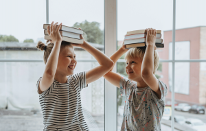 Zwei Kinder haben Bücher auf den Kopf und machen Faxen 
