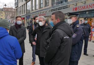 Fünf Menschen stehen in einer Straße mit vielen Läden, um Sie einige Polizisten und Journalisten