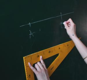 Zwei Hände halten ein Dreieck und schreiben eine geometrische Formel an die Tafel 