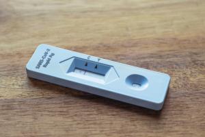 Ein länglicher Corona-Schnelltest aus weißem Plastik liegt auf einer Holzfläche