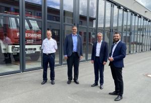 Vier Männer schauen in die Kamera, im Hintergrund ein Feuerwehrgebäude