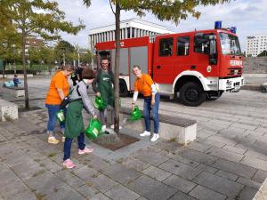 Vier Personen gießen einen Baum, im Hintergrund ein Feuerwehrwagen