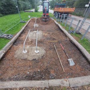 Einen Bagger auf einem sandigen Untergund davor liegen Gartengeräte