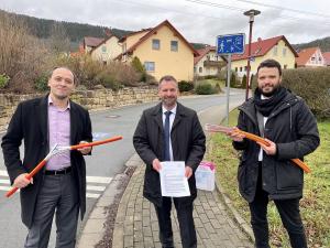 Drei Männer scheuen in die Kamera, im Hintergrund eine Siedlung mit Einfamilienhäusern