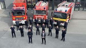 Feuerwehrleute in Uniform vor drei Feuerwehrfahrzeugen