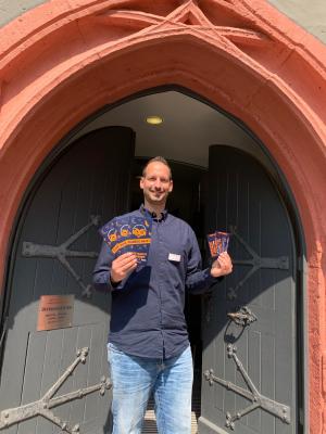 Christian Möller von den Städtischen Museen Jena steht vor einem Tor und hät Tickets in die Kamera.