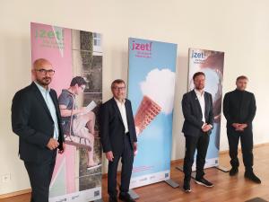 Vier Männer lächeln in die Kamera, im Hintergrund stehen Rollups.