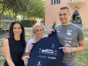 Drei Menschen lächeln in die Kamera und halten ein Oberteil mit Logos von Sponsoren hoch