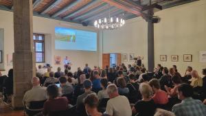 Bürgermeister Christian Gerlitz steht auf einer Bühne am Pult und begrüßt viele Menschen im Historischen Rathaus.