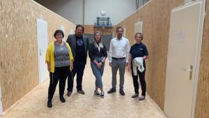 5 Personen in einer umgebauten Turnhalle schauen die Kamera