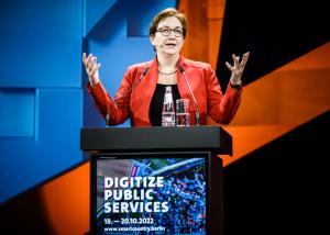 Poilikerin spricht hinter einem Thresen auf einer Bühne.