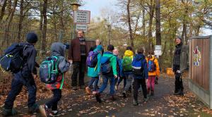 Grundschulkinder gehen durch ein geöffnetes Tor. 3 Erwachsene empfangen Sie.