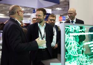 Vier Männer stehen an einem Stand auf einer Messe und unterhalten sich.