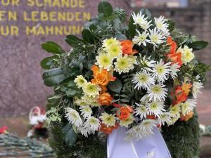 Ein Kranz mit Blumen vor einem Denkmal im Hintergrund