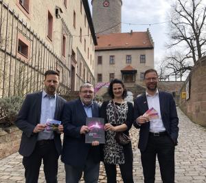 Drei Männer und eine Frau stehen vor der Leuchtenburg und halten Karten fpr die "Tage der Jenaer in der Hand"