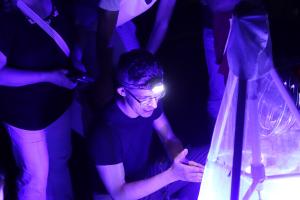 Ein Mann hockt vor einer einer Lichtfangstelle und erklärt etwas über eine angelockte Motte.