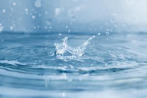 Ein Wassertropfen fällt in ein Glas Wasser. Wassertropfen spritzen weg.