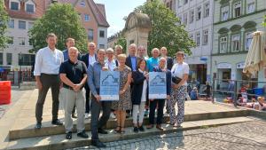 Bürgermeister Christian Gerlitz mit Sponsor*innen des Fassadenpreises stehen auf dem Jenaer Marktplatz am Brunnen.