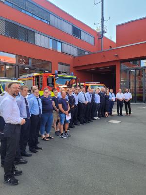 Gruppenbild der Fluthelfer*innen, Oberbürgermeister Thomas Nitzsche, Sicherheitsdezernent Benjamin Koppe und Oberbranddirektor Peter Schörnig vor Fahrzeugen des Katastrophenschutz