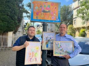 Zwei Männer zeigen Kunstwerke von Kindern