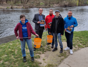 Vier Männer und eine Frau stehen an der Saale und halten Eimer, Müllzangen und Plakate